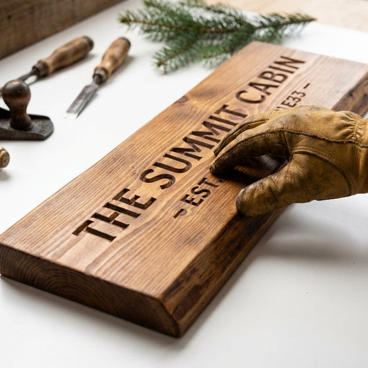 Handcrafted custom wood cabin sign being finished with tools and pine branch nearby