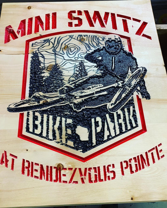 Custom wood sign with mountain biker, forest background, and text MINI SWITZ BIKE PARK at RENDEZVOUS POINTE.