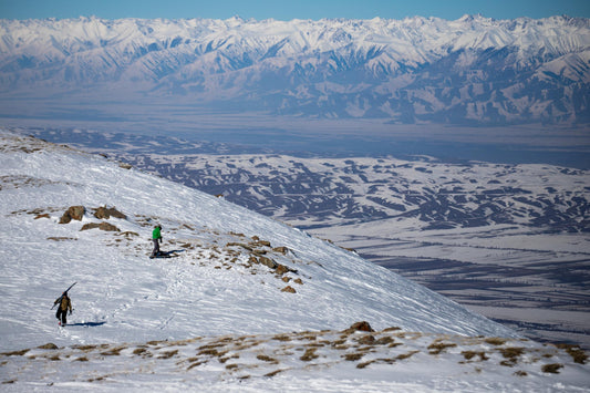 Two backcountry winter-sports visitors on an open snowy ridge above a broad valley, from the Winter Tourism Library's Jyrgalan collection.