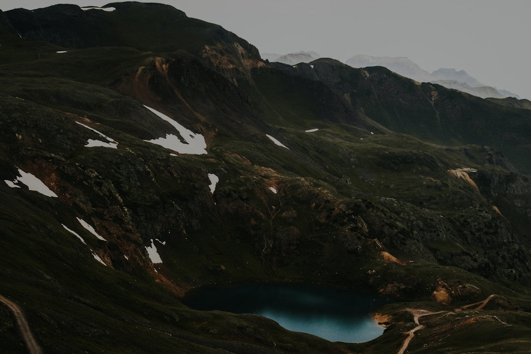 Mountain landscape with alpine lake, patches of snow, and rugged hiking trails