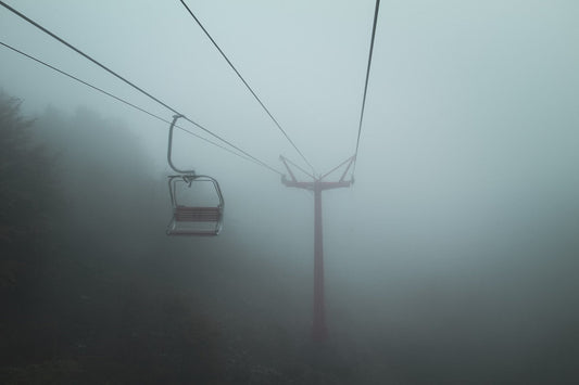 Lonely mountain ski lift in dense fog with trees barely visible below