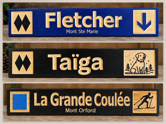 Three custom outdoor trail sign plaques displayed vertically on a wooden surface. The top plaque is blue with gold lettering reading 'Fletcher' and 'Mont Ste Marie', flanked by black-and-gold mountain symbols.