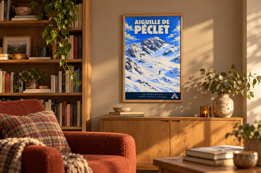 Aiguille de Péclet alpine art print in a natural oak frame above an oak cabinet, beside bookshelves and a rust-coloured armchair in a sunlit room.