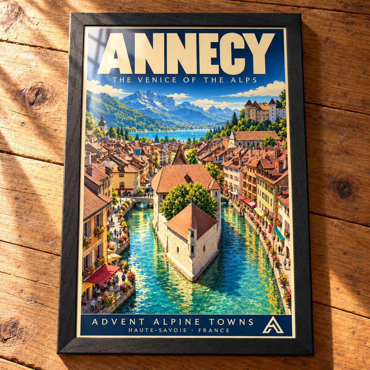 Complete Annecy framed art print in Black Ash on a timber tabletop, showing turquoise canals, old-town rooftops, a lake and mountains, with reflections across the glazing.