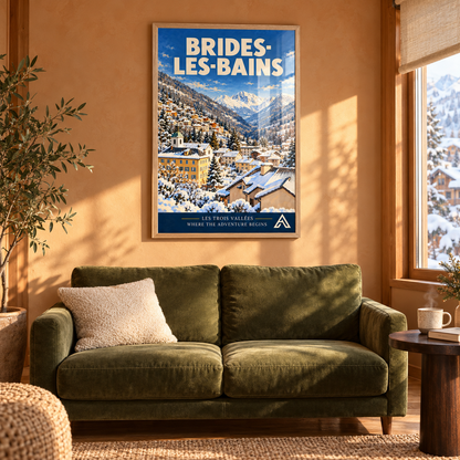 Brides-les-Bains art print in a natural oak frame above a green sofa in a sunlit alpine living room, showing a snowy valley town and mountain peaks.