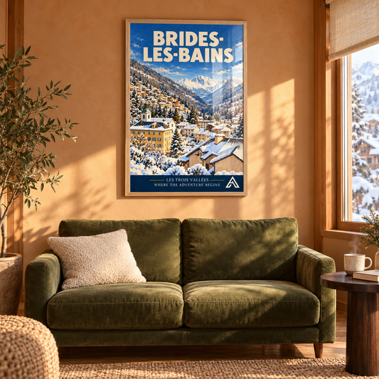 Brides-les-Bains art print in a natural oak frame above a green sofa in a sunlit alpine living room, showing a snowy valley town and mountain peaks.