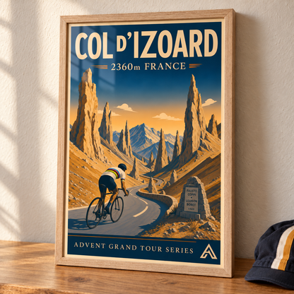 Col d’Izoard art print in a Natural Oak frame on a wooden tabletop beside a cycling cap, showing a cyclist wearing the white rainbow-banded world champion jersey.
