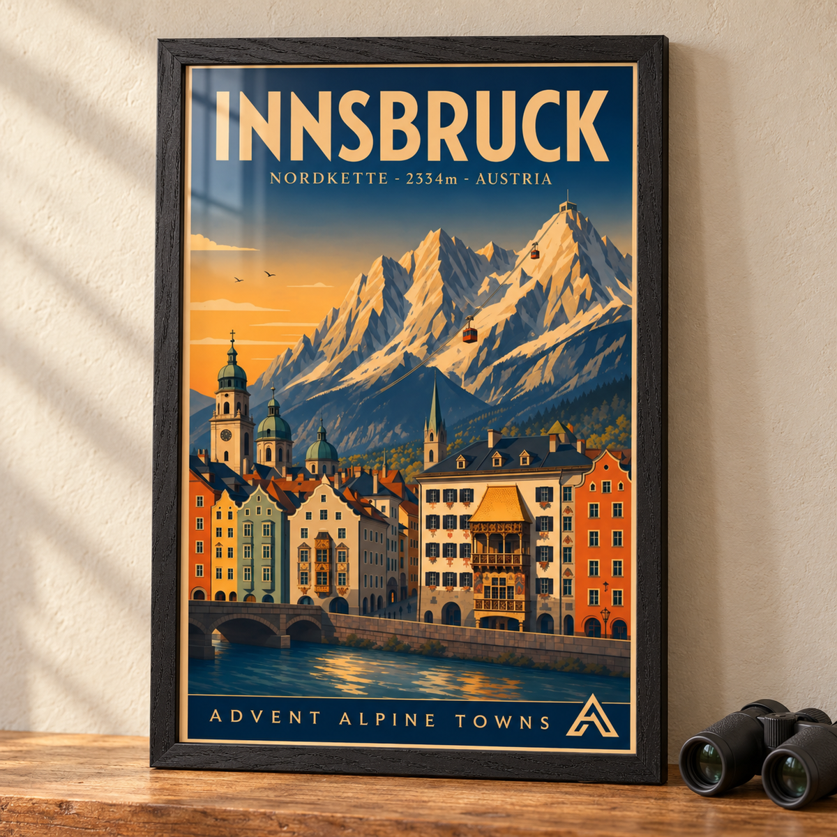 Innsbruck art print in a Black Ash frame on a wooden tabletop beside binoculars, showing the Inn River, Alpine architecture and Nordkette cable cars.