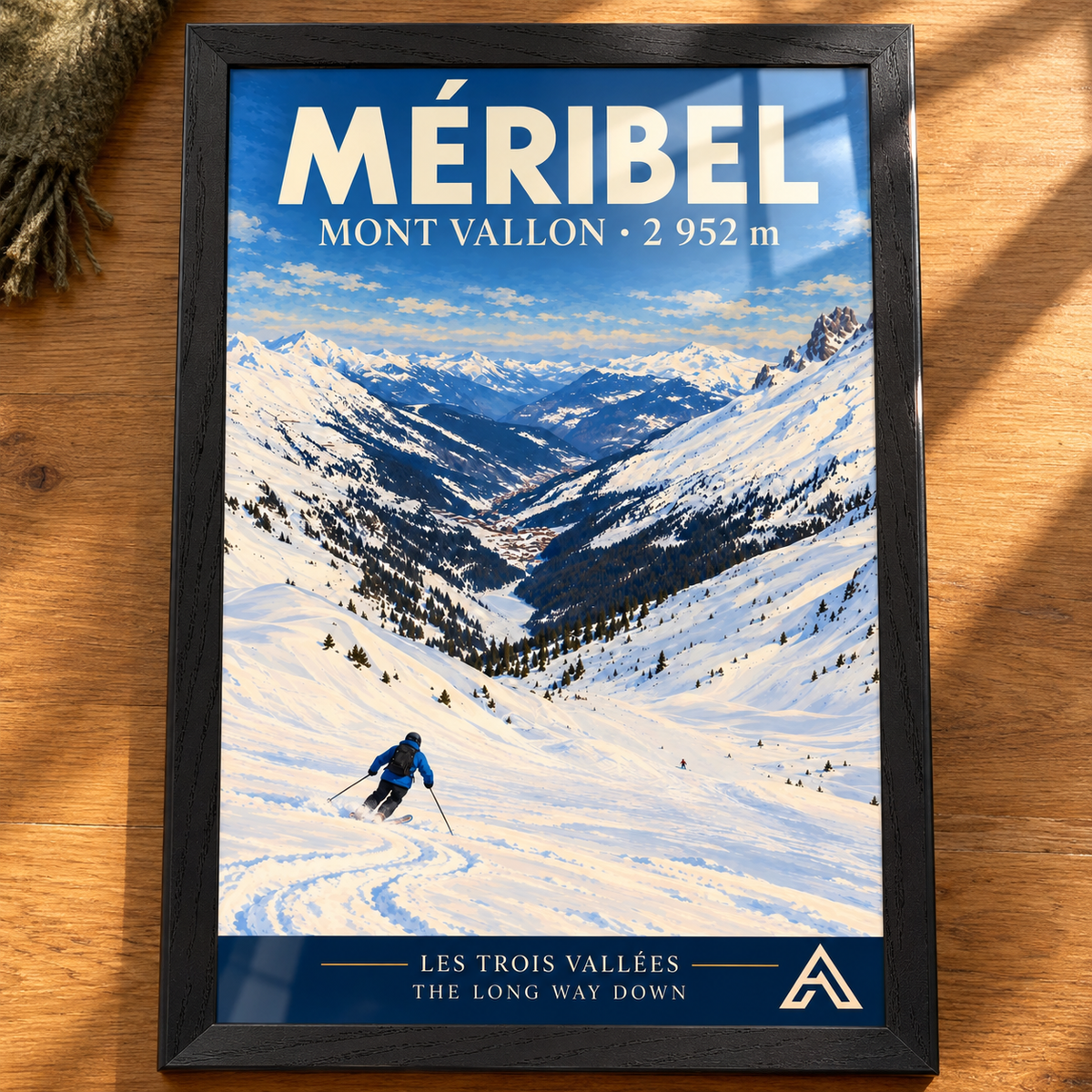 Complete Méribel Mont Vallon art print in Black Ash on an oak tabletop, showing a blue-jacketed skier descending towards a snowy Alpine valley, with sunlight and window reflections on the glass.