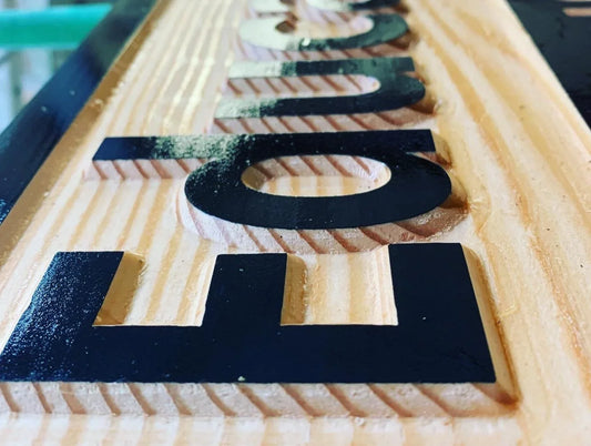 Close-up of engraved wood sign with bold black lettering on natural spruce
